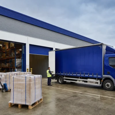 A UK logistics site receives overflow pallets beside open loading bays and a right-hand drive rigid vehicle.