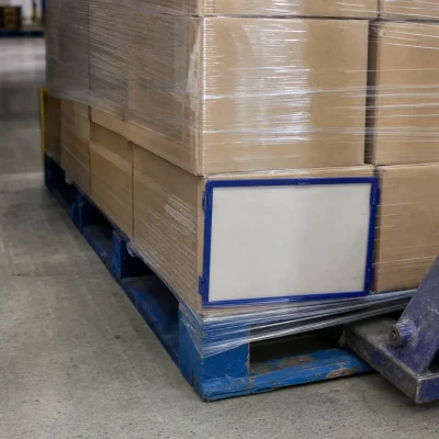 A wrapped reserve pallet and pallet truck wheel sit beside a narrow aisle in a UK warehouse storage area.