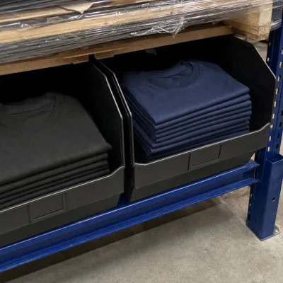 Separate storage bins hold black and navy T-shirts in a warehouse aisle, illustrating SKU differences.
